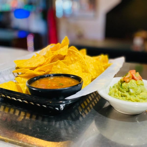 A basket of tortilla chips with salsa and a bowl of guacamole with diced tomatoes.