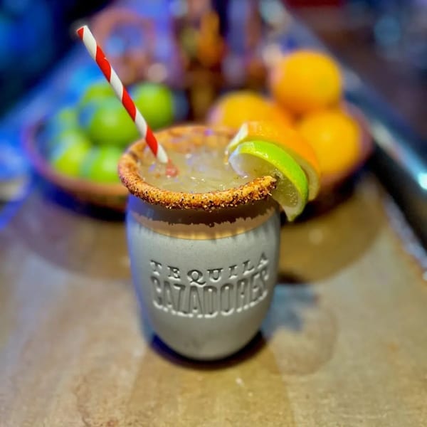 A Tequila Cazadores cocktail with a chili-lime rim, lime slices, and a red-and-white straw.
