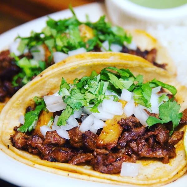 Two Villa Escondida tacos with meat, cilantro, and diced onions on a white plate.