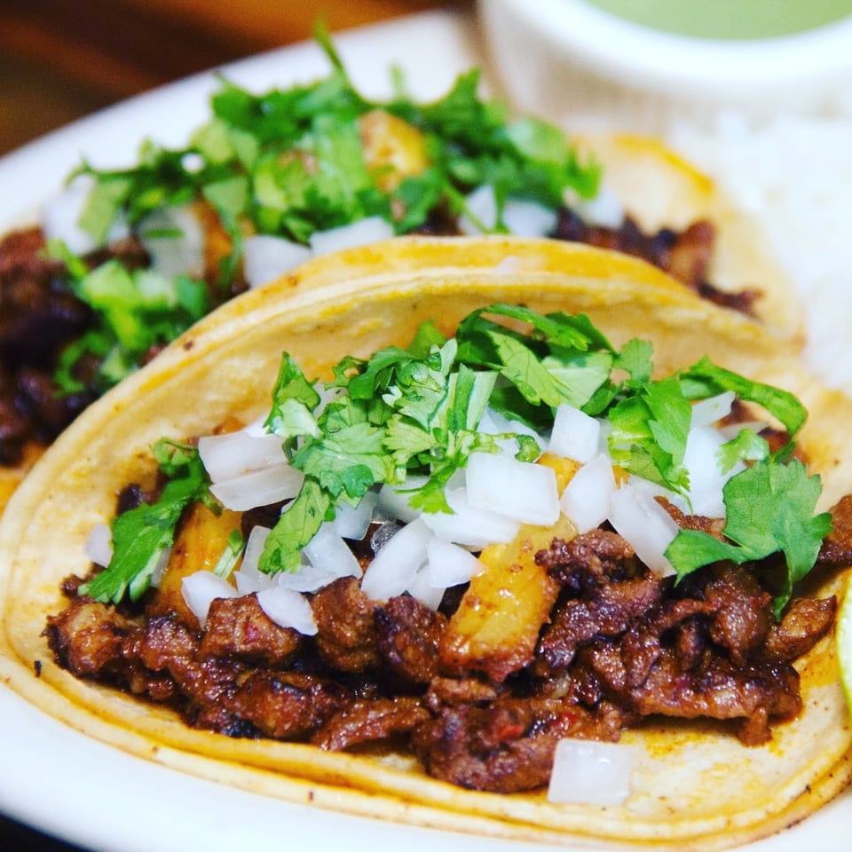 Two Villa Escondida tacos with meat, cilantro, and diced onions on a white plate.