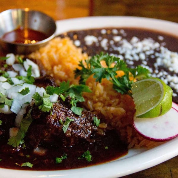 Mexican dish with dark meat, rice, black beans, cilantro, onions, lime, and radish.